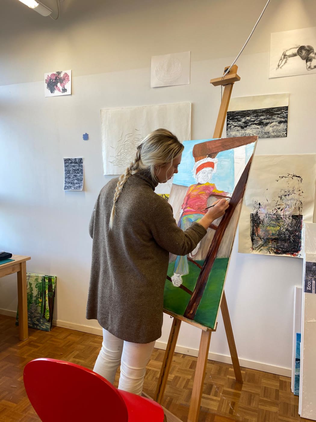 Corinna Haas at the easel, painting a figure in red and white
